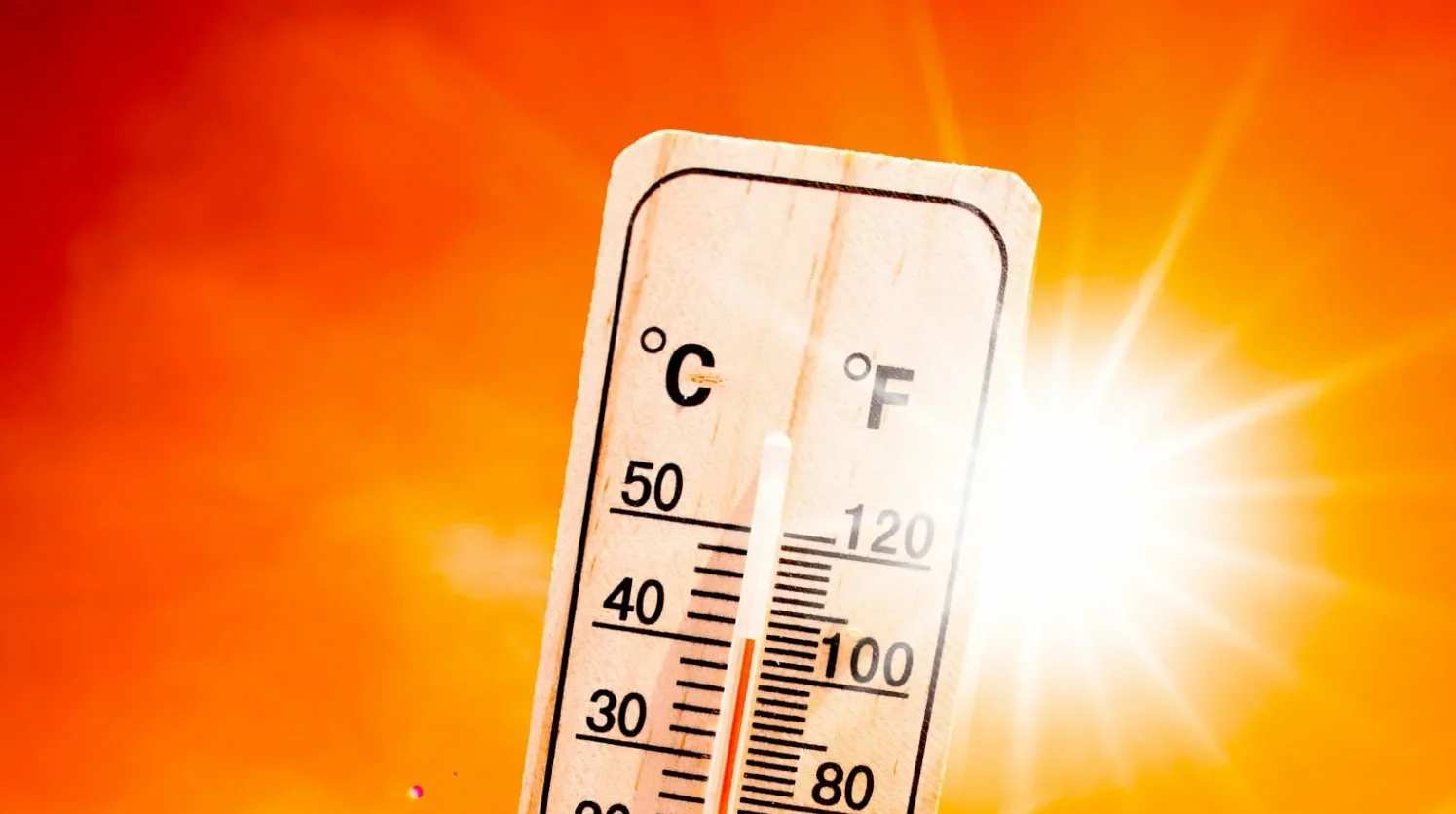 Un termometro indica unalta temperatura su uno sfondo rosso e arancione intenso, con un brillante sole che splende in alto a destra.